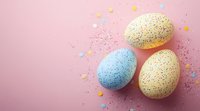 Speckled Easter eggs in pastel blue and yellow colors decorated with confetti on pink background. Festive spring holiday celebration composition.