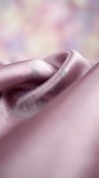 Soft pink silk fabric with elegant folds and gentle draping on blurred pastel background for luxury textile and fashion design projects.
