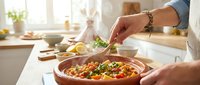 Person adding fresh herbs to homemade pasta dish in modern kitchen. Hands garnishing Italian meal with basil leaves for family dinner preparation.