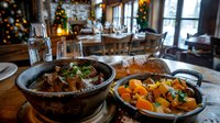 Rustic restaurant interior with two cast iron skillets serving beef stew and roasted vegetables, holiday decorations, warm lighting, fine dining ambiance.