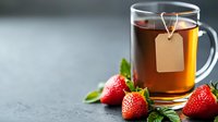 Glass cup of hot tea with blank label teabag and fresh ripe strawberries on dark background with copy space. Healthy organic beverage concept.