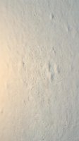 Rough textured white plaster wall surface with natural imperfections and subtle shadows creating depth for interior design backgrounds.