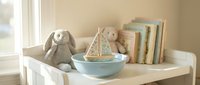 Cozy nursery shelf with soft plush toys, wooden sailboat in ceramic bowl and pastel books creating peaceful childhood decor for baby room design.