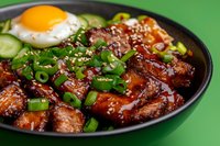 Glazed pork belly with sunny side up egg, garnished with green onions and sesame seeds in Asian style bowl, served on vibrant green background.