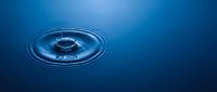 Water droplet creating concentric ripples on blue surface, suitable for backgrounds, environmental concepts, and liquid dynamics illustrations.