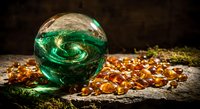 Green crystal ball with swirling patterns surrounded by amber gemstones on rustic wooden surface for fortune telling and mystical divination practices.