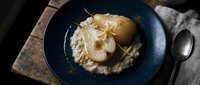 Sliced pears arranged on creamy puree with powdered sugar garnish, plated on dark blue dish for fine dining presentation.