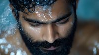 Close-up portrait of bearded Middle Eastern man with water droplets on face and closed eyes against turquoise background, expressing serenity and wellness.