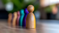 Wooden game piece stands in focus while colorful figures blur into background, symbolizing leadership, individuality and standing out from crowd in business concept.