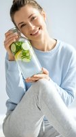 Young woman of mixed ethnicity holding infused water with cucumber and lemon slices, promoting healthy hydration and wellness lifestyle choices.