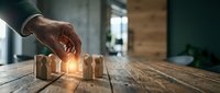 Professional businessman hand selecting glowing wooden figure from group on rustic table, representing leadership choice and human resources management.