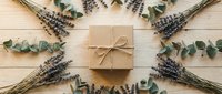 Kraft paper gift box with natural twine bow surrounded by dried lavender stems and eucalyptus leaves on wooden background for eco-friendly packaging design.