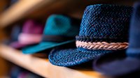 Stylish woven straw fedora hats in navy blue and teal colors with braided leather bands displayed on wooden shelf, selective focus on detailed texture.