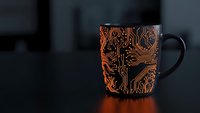 Black coffee mug with orange circuit board pattern design on dark background, technology themed drinkware for office and tech enthusiasts.
