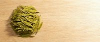 Dried green tea leaves arranged on wooden surface, suitable for beverage packaging, wellness content, and culinary publications.