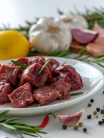 Fresh raw beef chunks on white plate with rosemary, garlic, chili pepper and spices. Close up view of meat preparation for cooking or grilling.