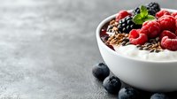 Fresh yogurt bowl with raspberries, blueberries, dark chocolate shavings and mint leaves on gray concrete background, selective focus, copy space.