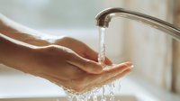Hands cupped under running water from modern faucet in bright bathroom. Clean fresh water flowing into palms for washing and hygiene routine.