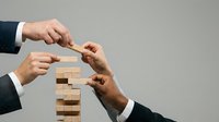 Business teamwork concept with hands building wooden block tower together representing collaboration and strategic planning in corporate environment.
