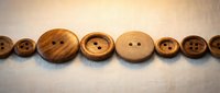 Wooden buttons in various sizes arranged in a row on neutral fabric background, suitable for fashion, sewing, and craft projects.