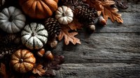 Rustic autumn arrangement with decorative pumpkins, pine cones, acorns and dried oak leaves on weathered wooden background.