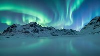 Spectacular aurora borealis dancing over snow-covered mountain peaks in arctic wilderness during polar night creating magical winter landscape.