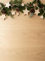 Festive holiday border with wooden stars, evergreen branches, pinecones, and berries arranged on light wood surface. Ideal for seasonal greeting cards and holiday marketing materials.