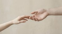Two hands reaching toward each other against a neutral beige background, symbolizing connection, support, and human touch.
