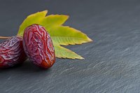 Fresh dates with green leaves on dark slate surface for healthy eating and natural food concepts.