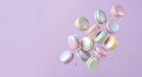 Colorful French macarons scattered on soft pink background with copy space for bakery and dessert design projects.