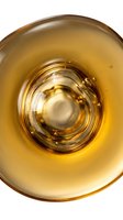 Overhead view of golden liquid in glass bowl with concentric ripples, isolated on white background for culinary and beverage design projects.