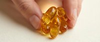 Close-up of hand holding golden amber gel capsules on neutral background, suitable for health, wellness, supplement and pharmaceutical marketing materials.
