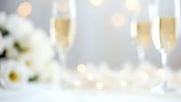Elegant champagne flutes filled with sparkling wine on white table with soft bokeh lights and white flowers creating romantic celebration atmosphere.