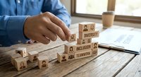 Business professional building wooden blocks with diversity, inclusion and teamwork text in modern office workspace for corporate strategy planning.