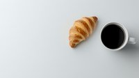 Fresh baked croissant and cup of black coffee on white background, minimalist breakfast composition with copy space for menu design or food blog.