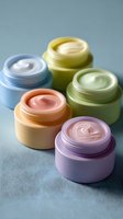 Colorful cosmetic cream jars in pastel shades of blue, yellow, peach, green, and purple arranged on light blue background for beauty product advertising.