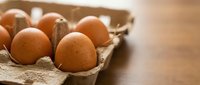 Fresh brown eggs in cardboard carton on wooden table surface for cooking and baking recipes.