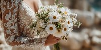 Bride in elegant lace dress holding white daisy bouquet with baby's breath for wedding ceremony celebration.