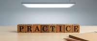 Wooden letter blocks spelling PRACTICE on desk under modern LED light fixture in minimalist office workspace for business training concepts.