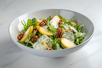 Fresh pear and gorgonzola salad with arugula, pecans and honey dressing served in white bowl on marble surface, restaurant quality food styling.