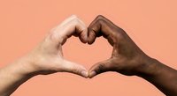 Two diverse hands forming heart shape symbol representing unity love and friendship on coral background.