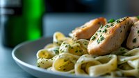 Creamy fettuccine pasta with grilled chicken breast slices and fresh herbs in butter garlic sauce, served on gray ceramic plate. Close-up with selective focus.