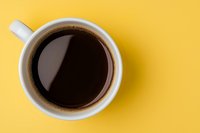 White ceramic cup filled with black coffee on vibrant yellow background, view from above. Minimalist composition with copy space for text or design.