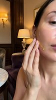 Young woman applying facial oil serum in luxury hotel room with warm lighting. Skincare routine, beauty treatment, wellness lifestyle concept.