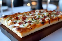 Freshly baked flatbread topped with melted mozzarella, crispy bacon bits, and caramelized onions served on wooden board, close-up view showing texture and toppings.