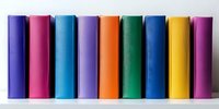 Colorful hardcover books arranged in row on white shelf, spines showing vibrant rainbow colors including blue, pink, purple, orange, green and yellow. For education or library design.