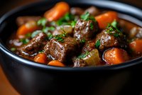 Hearty beef stew with tender meat chunks, bright carrots and fresh herbs in dark ceramic bowl, rich brown gravy sauce. Close up with selective focus.