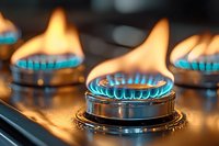 Blue gas flames burning on modern stove burner, close up view with selective focus showing kitchen appliance detail in warm orange glow.