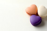Heart-shaped macarons in pastel peach, white, and purple colors arranged on white wooden background, creating romantic minimalist composition for Valentine's day designs.