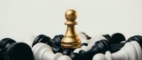 Golden pawn chess piece standing victorious among fallen black and white pieces on neutral background symbolizing leadership and strategic success.